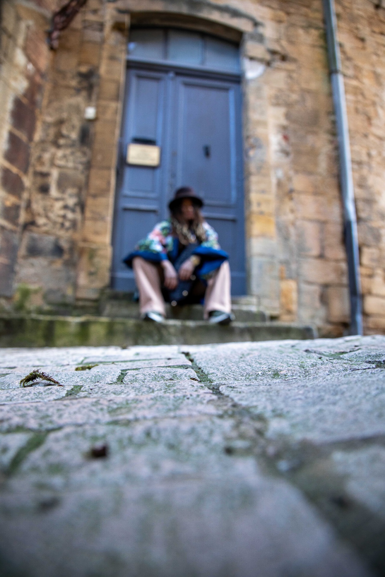 Traciana seated on stone steps before a blue door in Sarlat, France